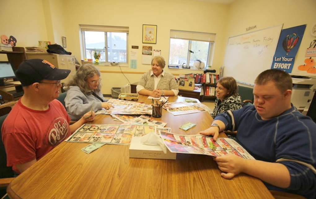 adults seated around a central table studying worksheets about money, prices, and household budgets