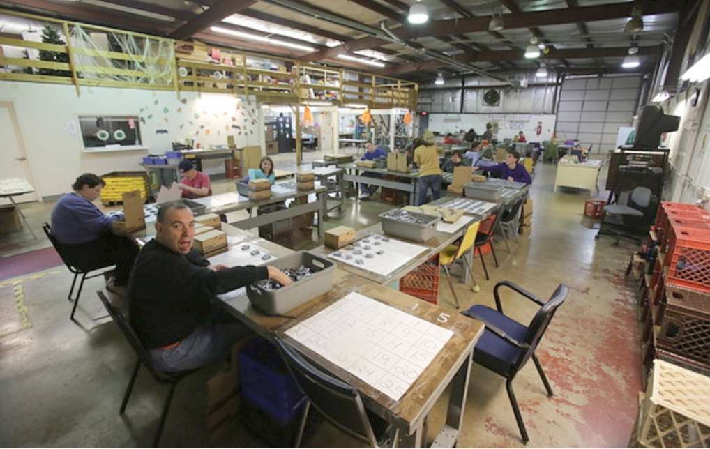 adult workers seated at tables with sorting sheets and boxes of items to sort